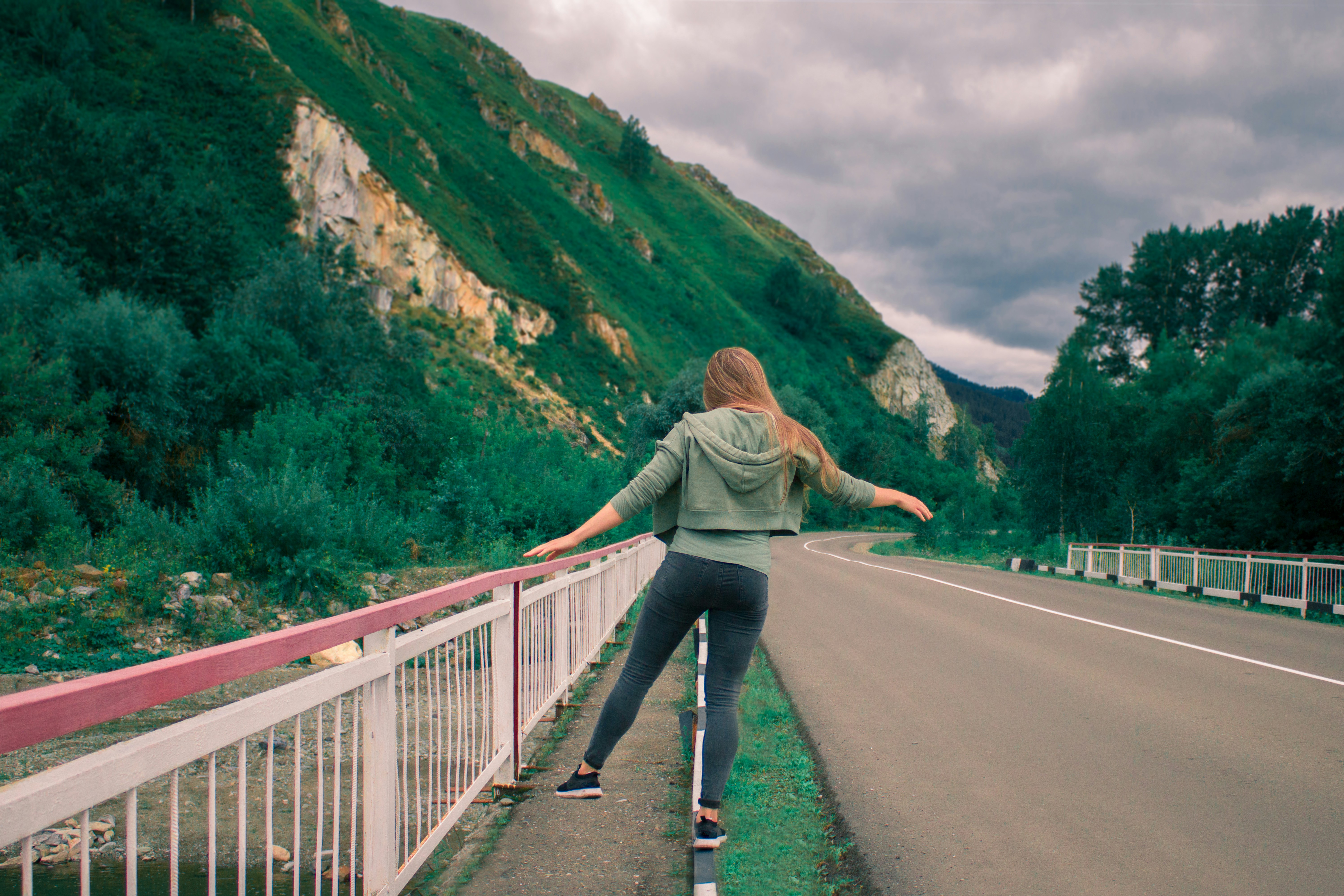 woman in gray jacket and blue denim jeans walking on gray concrete bridge during daytime