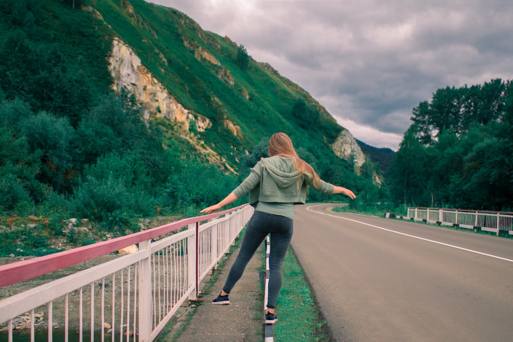 woman in gray jacket and blue denim jeans walking on gray concrete bridge during daytime