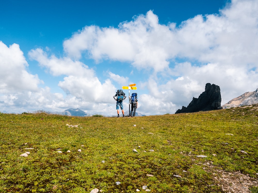 people hiking on green grass field under white clouds and blue sky during daytime