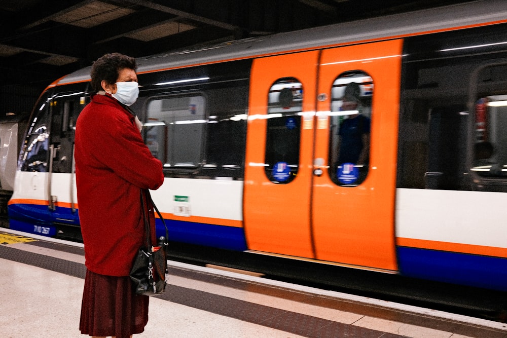 woman in red coat standing beside blue and yellow train during daytime