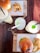 A wooden table holds two wooden serving boards, each with a burger and a side of potato wedges. Three different beverages in tall glasses are present, garnished with lime and mint, and varying in straw colors.