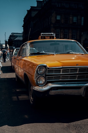 A neat yellow taxi parked outside a charming Dundee street with historic buildings in the background.