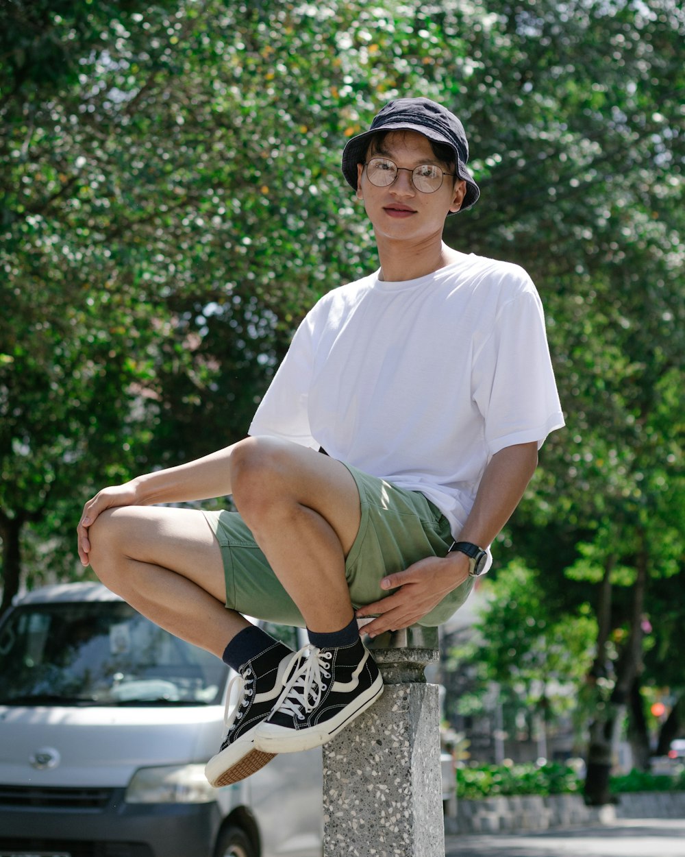 man in white crew neck t-shirt and black and white nike shoes sitting on concrete