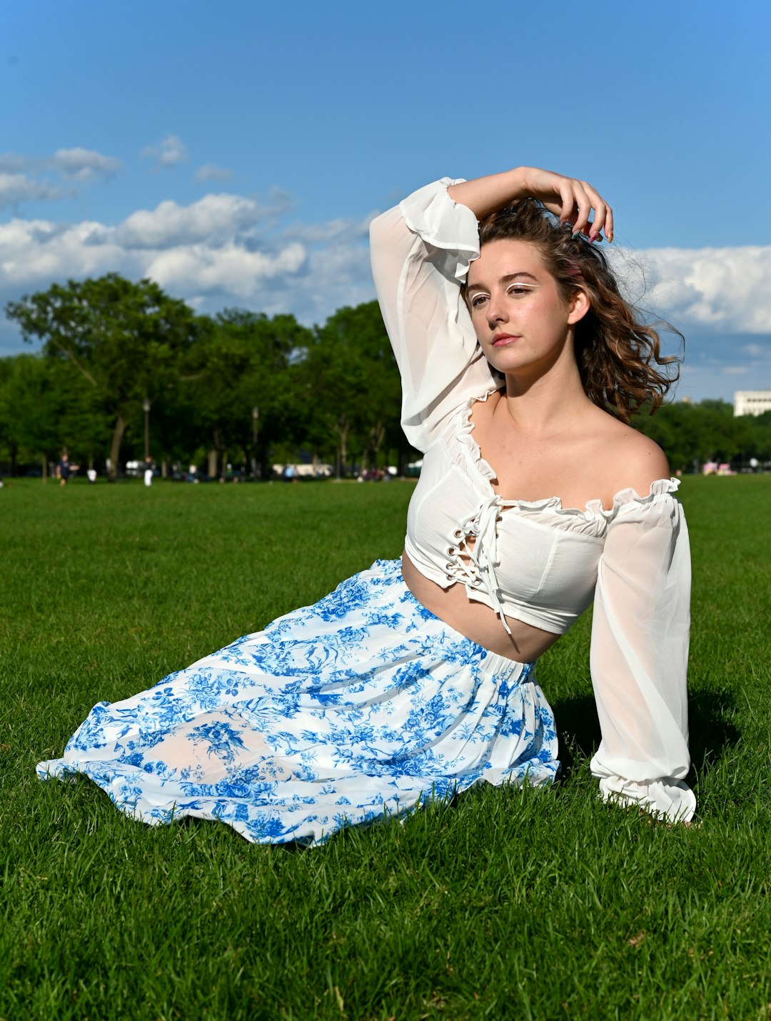 woman in white and blue floral dress lying on green grass field under blue sky during