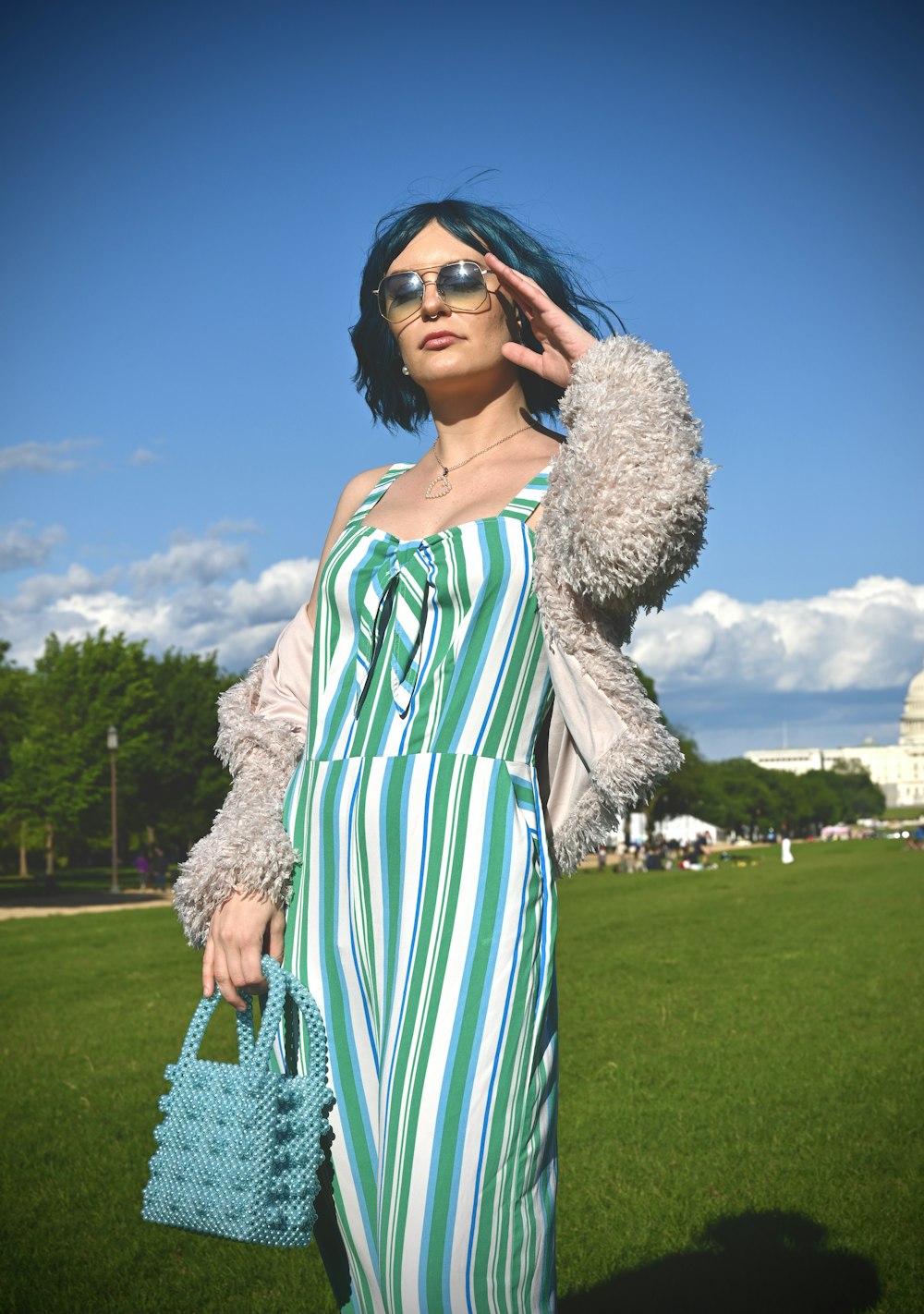 mulher no vestido branco e verde vestindo óculos de sol pretos em pé no campo de grama verde durante o dia