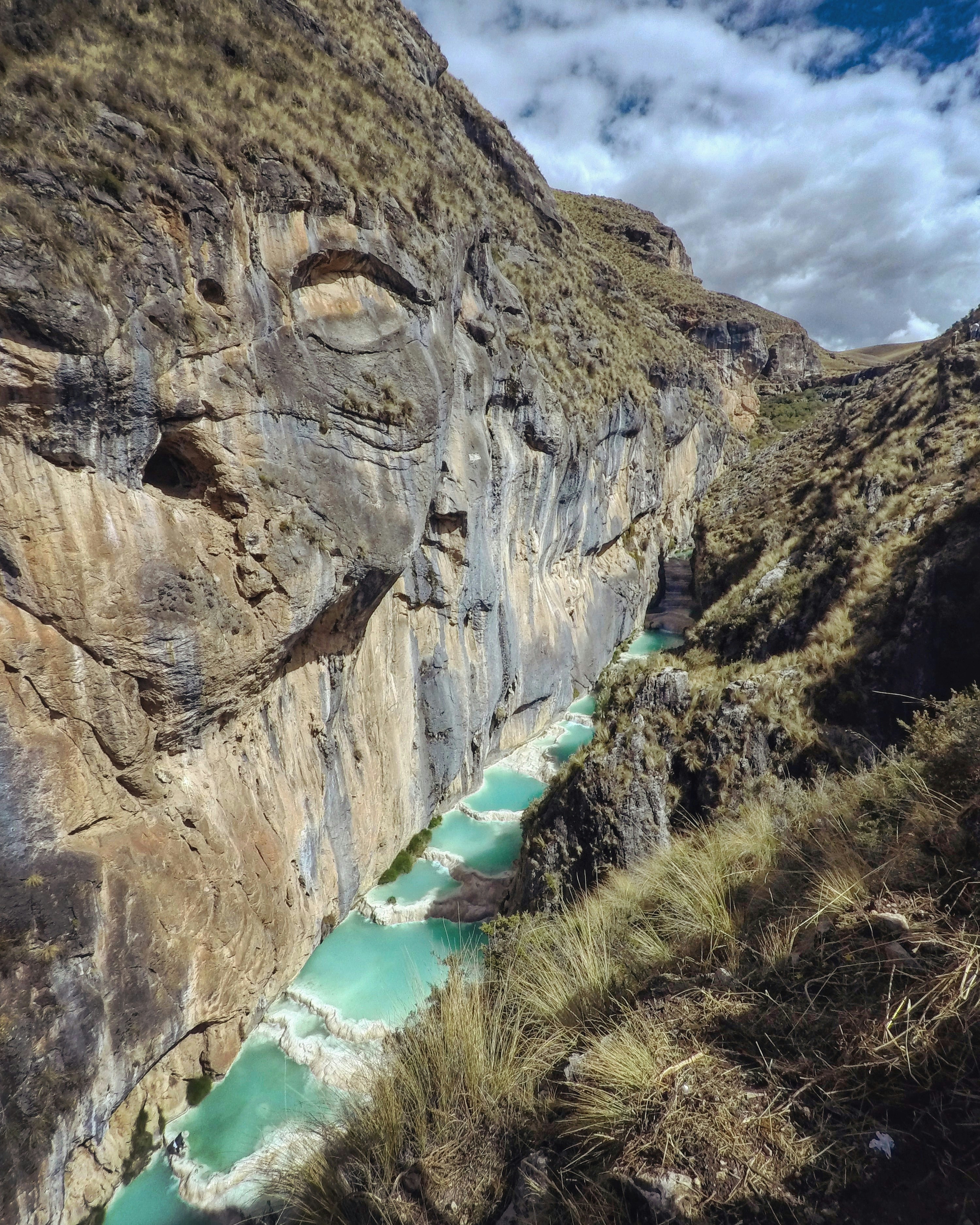brown rocky mountain beside river under white clouds during daytime