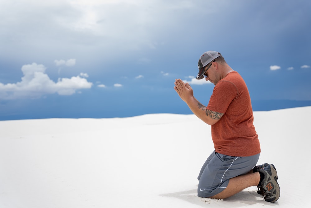 주황색 폴로 셔츠와 파란색 데님 반바지를 입은 남자가 낮에 하얀 모래 위에 앉아 있다