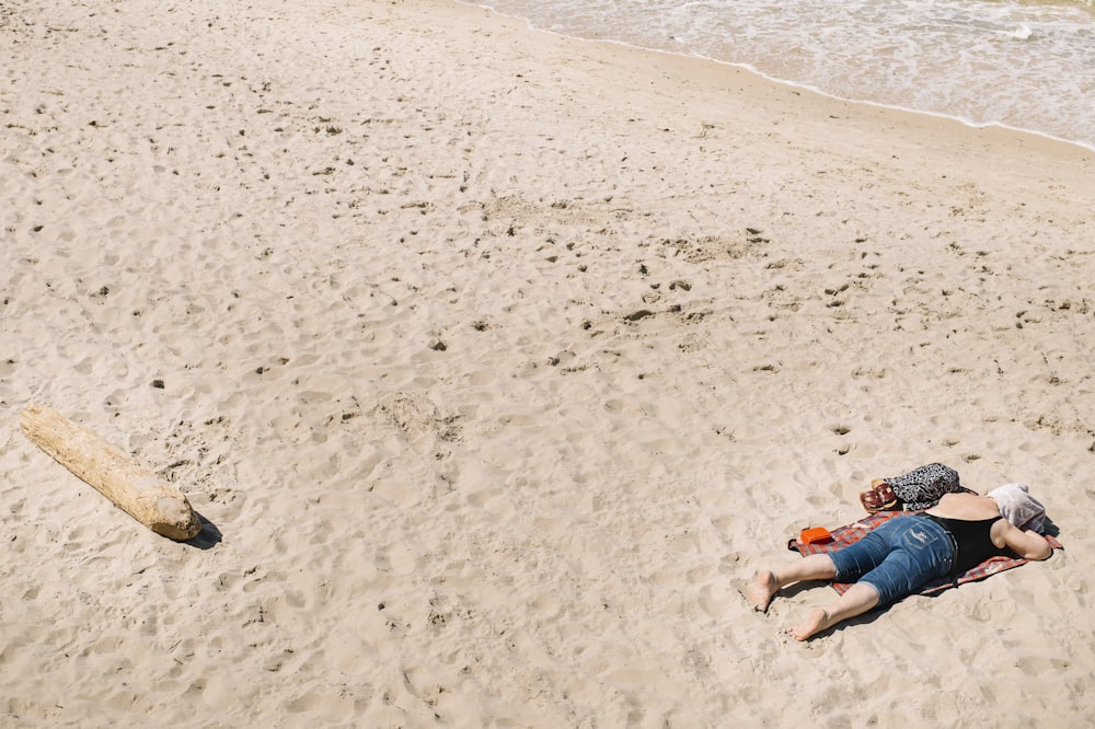 mulher em shorts jeans azuis deitados na areia da praia durante o dia