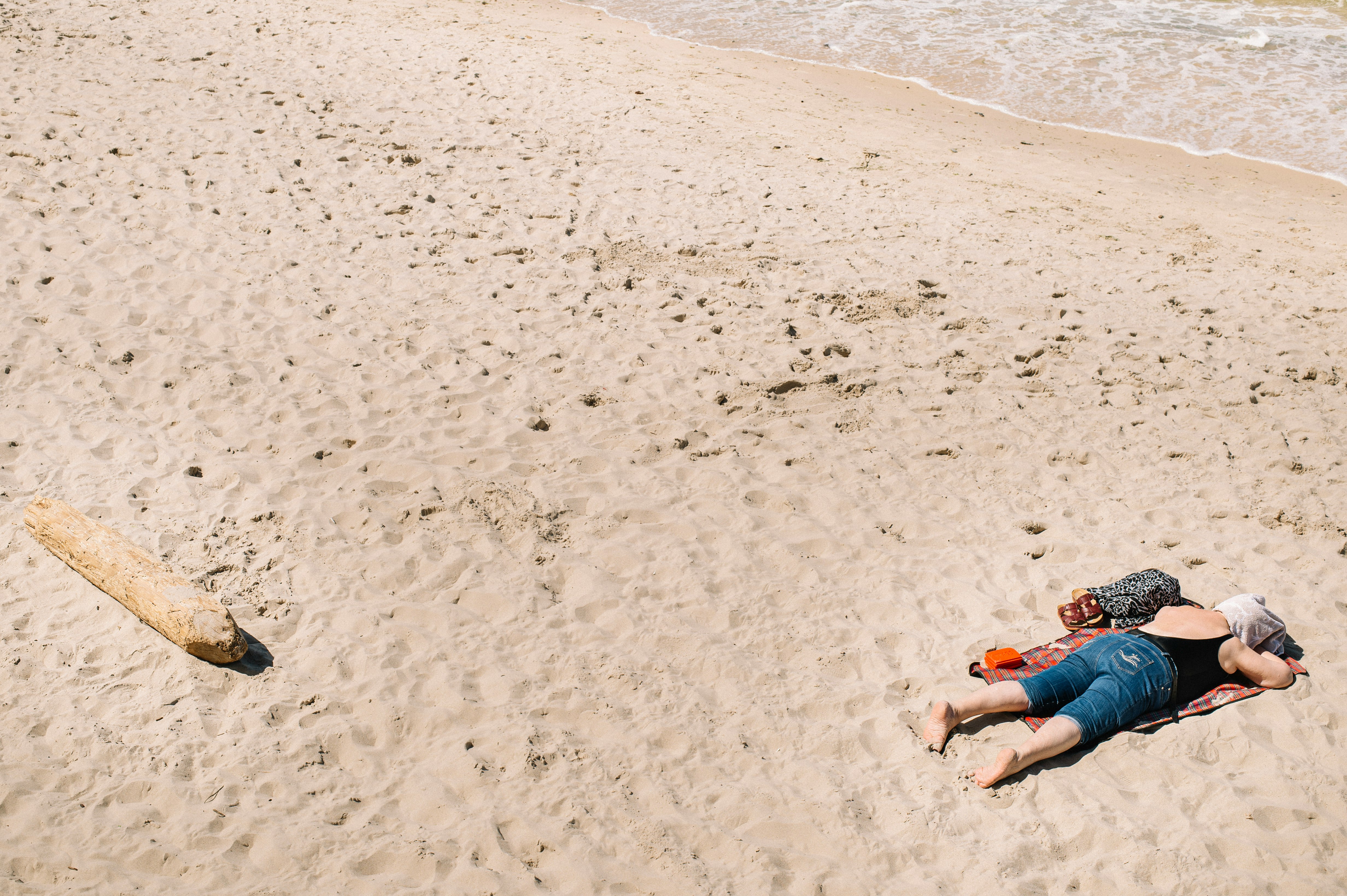 woman in blue denim shorts lying on beach sand during daytime