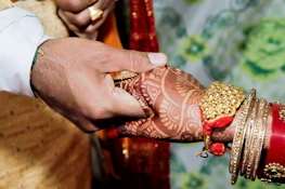 A close-up of intertwined hands adorned with wedding rings and henna designs.