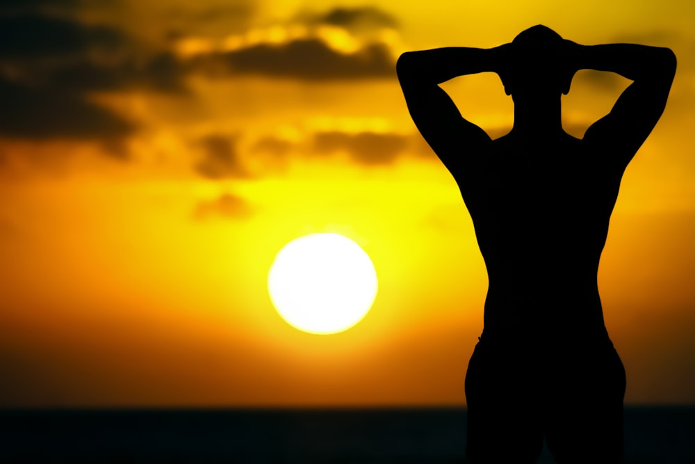 silhouette of man raising his hand during sunset