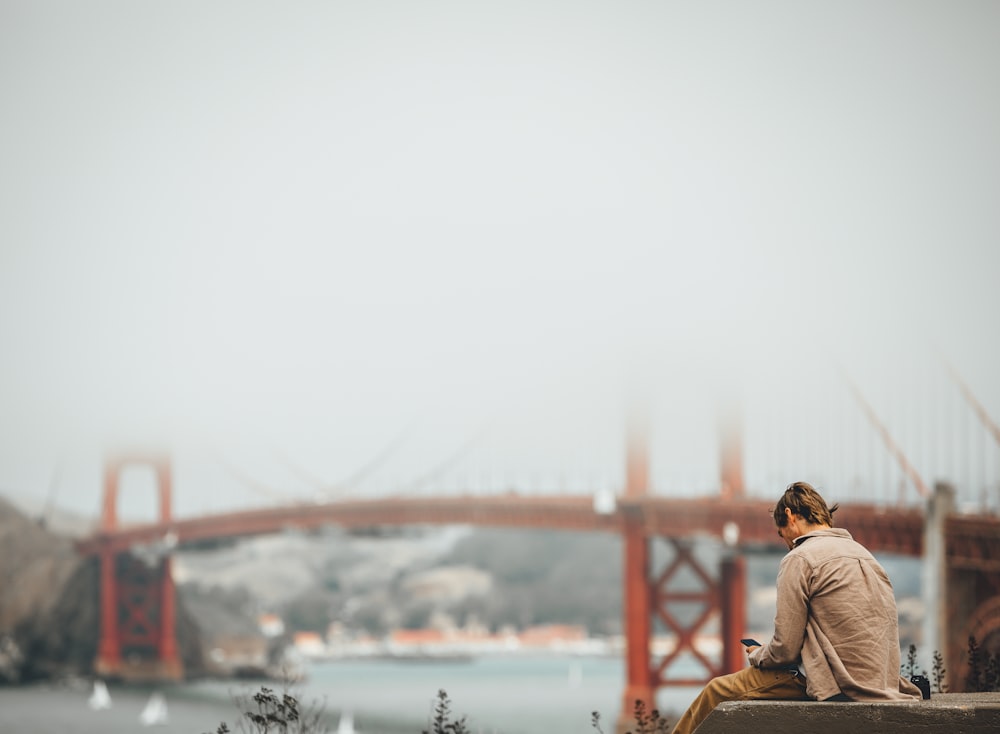 man and woman sitting on brown wooden bench near body of water during daytime