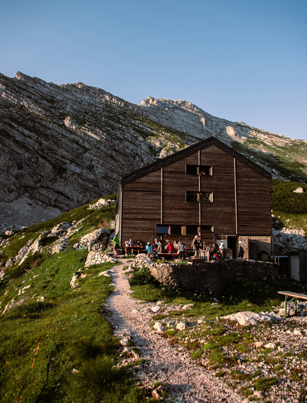 brown wooden house on green grass field near rocky mountain during daytime