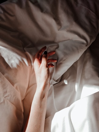 Close-up of a delicate hand resting on black silk sheets with crimson accents.