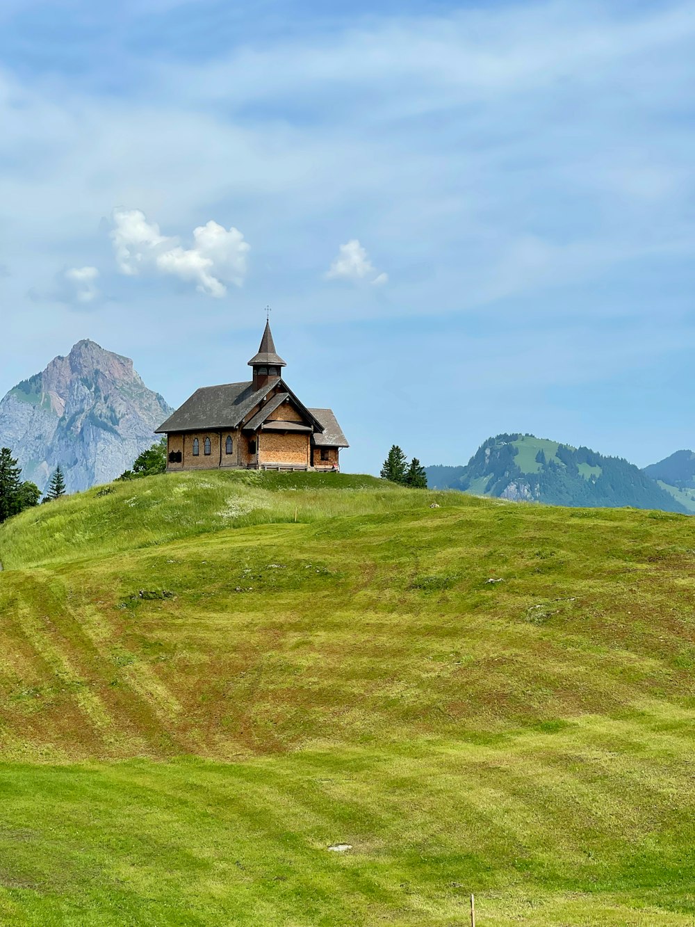 Braunes und schwarzes Haus auf grünem Grasfeld in der Nähe von Berg unter weißen Wolken während des Tages