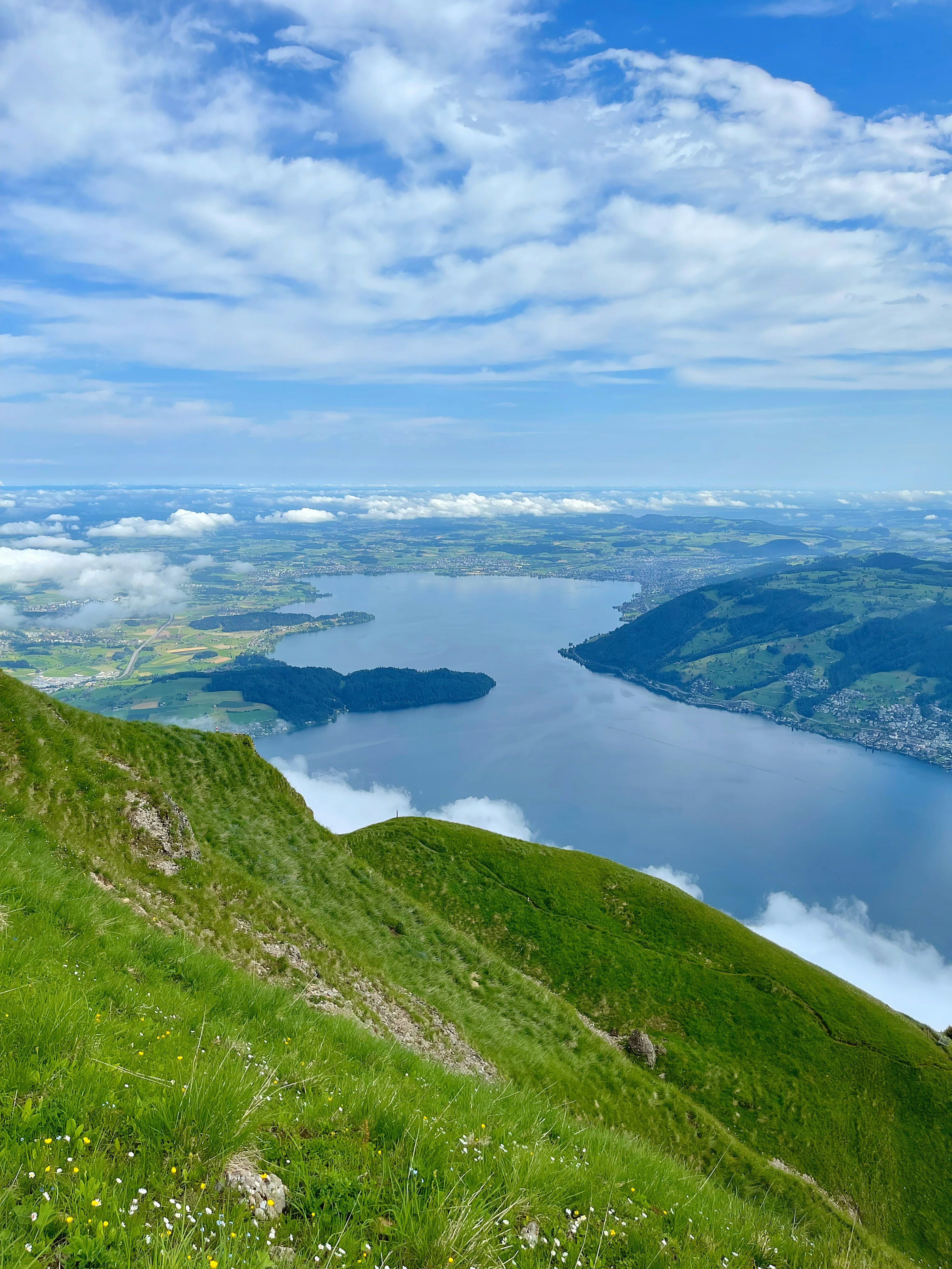 green-grass-covered-mountain-near-lake-under-white-clouds-and-blue-sky