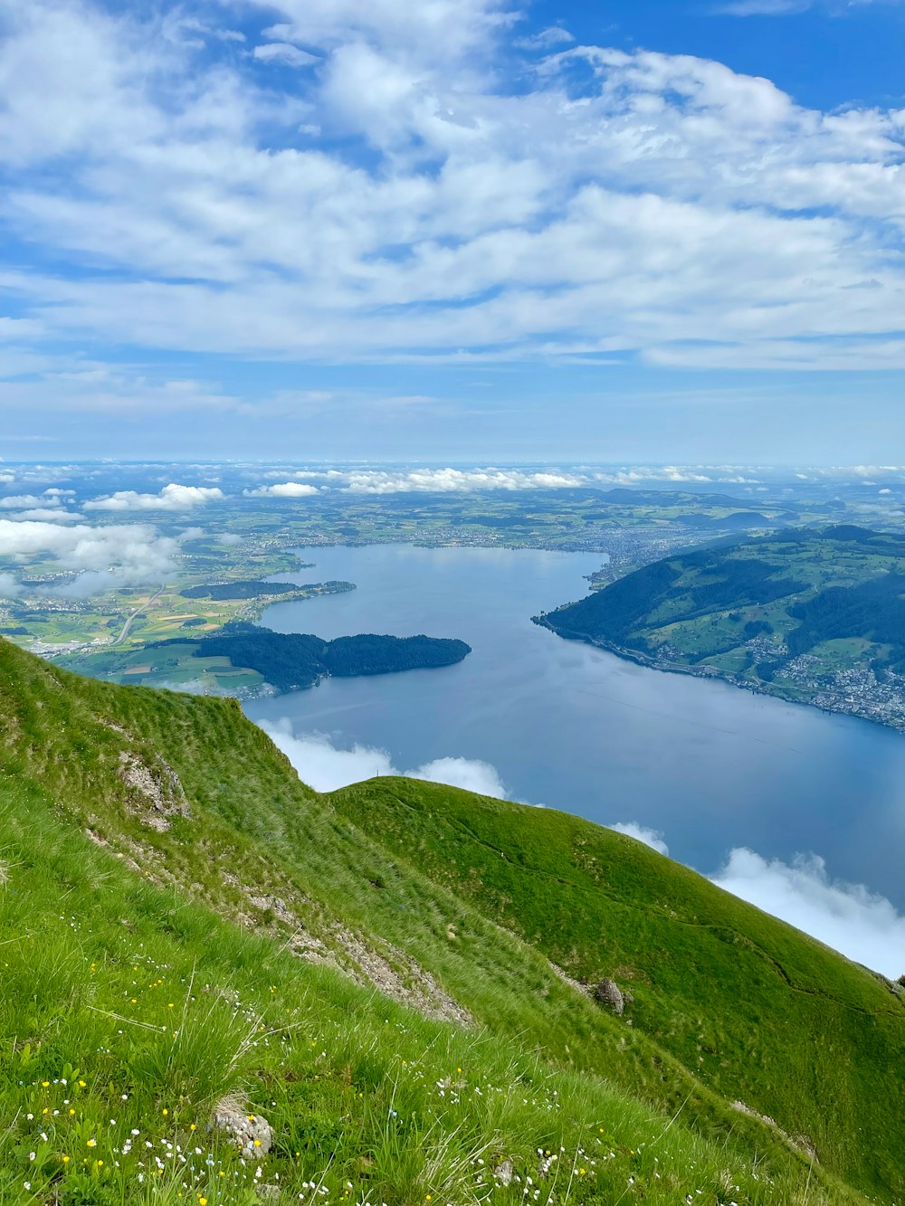 green grass covered mountain near lake under white clouds and blue sky during daytime