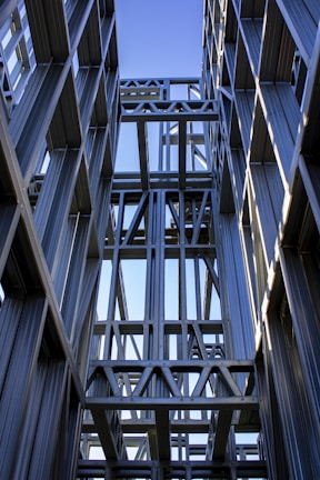 Steel structural beams arranged outdoors under a clear blue sky.