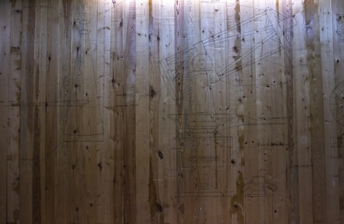 A wooden wall displays intricate line drawings of mechanical structures, possibly components of a telescope. The drawings include labeled parts, meticulously detailed in a technical style.
