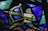 A vibrant stained glass artwork featuring geometric shapes and a variety of colors. The pieces are arranged in an abstract pattern, with overlapping layers of textured glass creating dynamic visual interest.