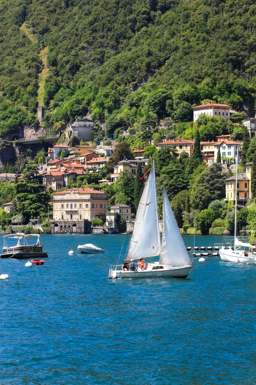 white sail boat on body of water near green mountain during daytime