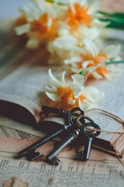 white and yellow flower on book page with four keys laying on the end of the page.