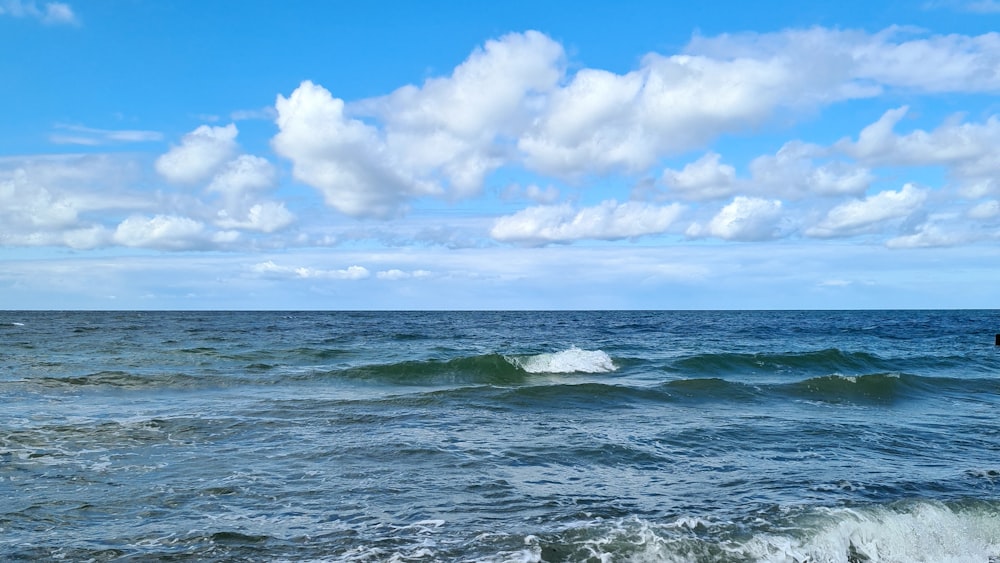ocean waves under blue sky and white clouds during daytime