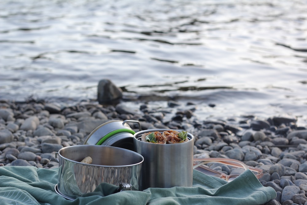 stainless steel bucket on gray rocks near body of water during daytime