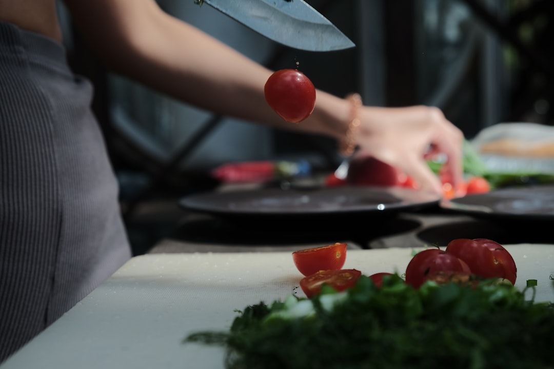 person slicing tomato on white chopping board