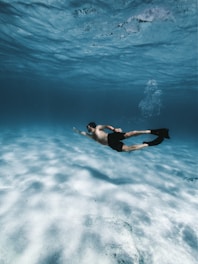 A swimmer wearing sleek swim fins gliding through clear blue water.