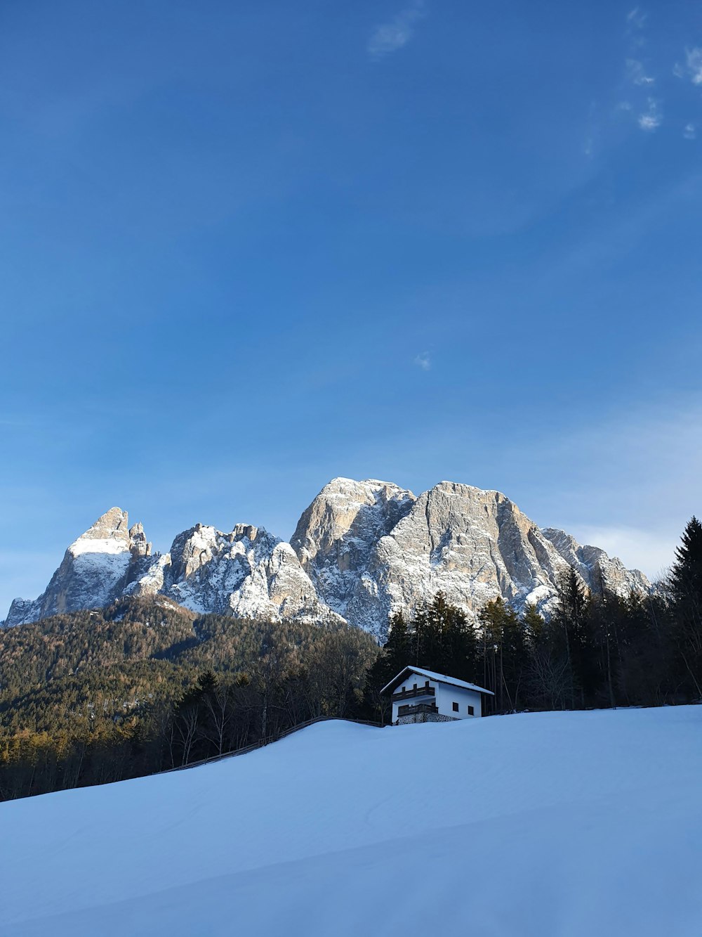 white and brown house on snow covered ground near rocky mountain under blue sky during daytime