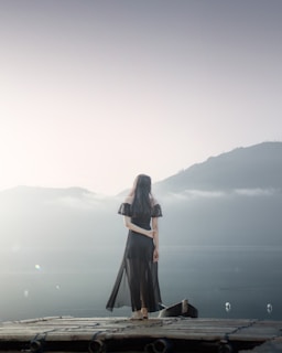 woman in black dress standing on brown wooden dock during daytime