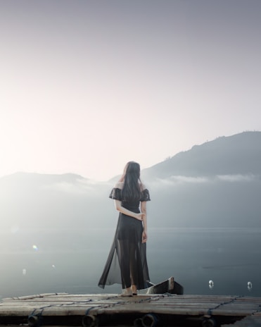 woman in black dress standing on brown wooden dock during daytime
