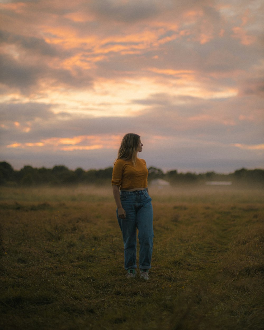 woman in blue denim jeans standing on green grass field during daytime