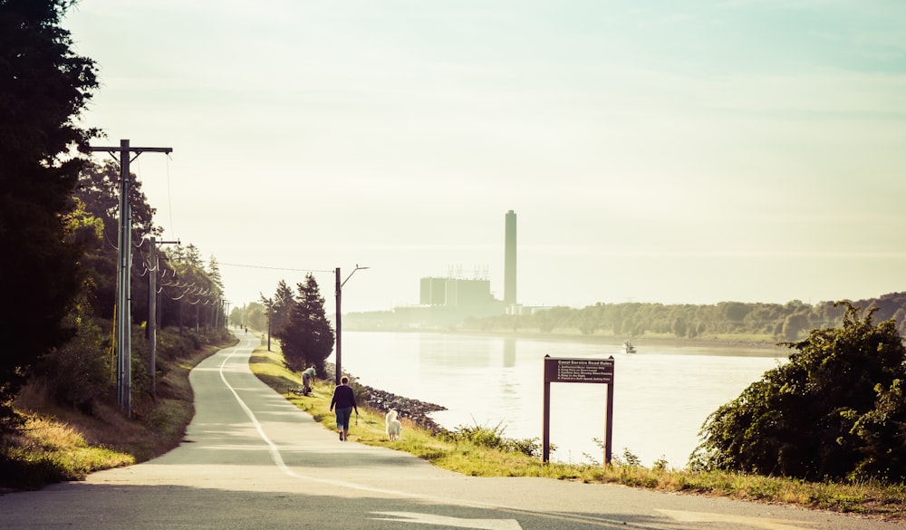 person in black jacket and pants walking on sidewalk near body of water during daytime