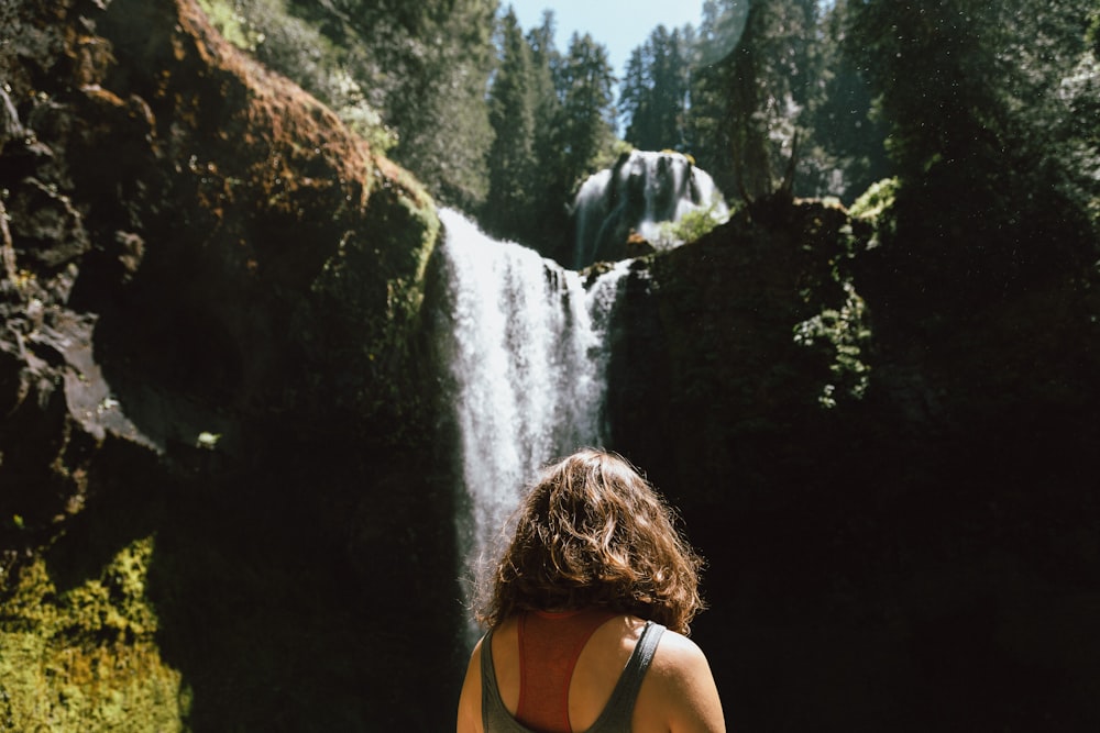 mulher na camiseta preta do tanque em pé perto das cachoeiras durante o dia