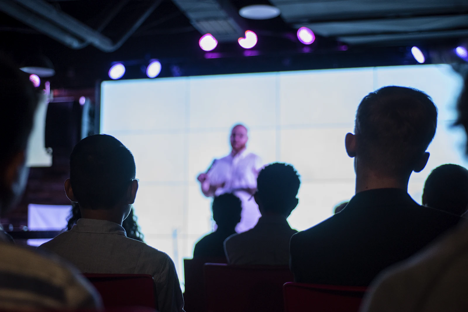 An audience watching a speaker in a darkened room