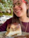 A smiling customer holding a slice of shepherd's cake with a cozy kitchen background.