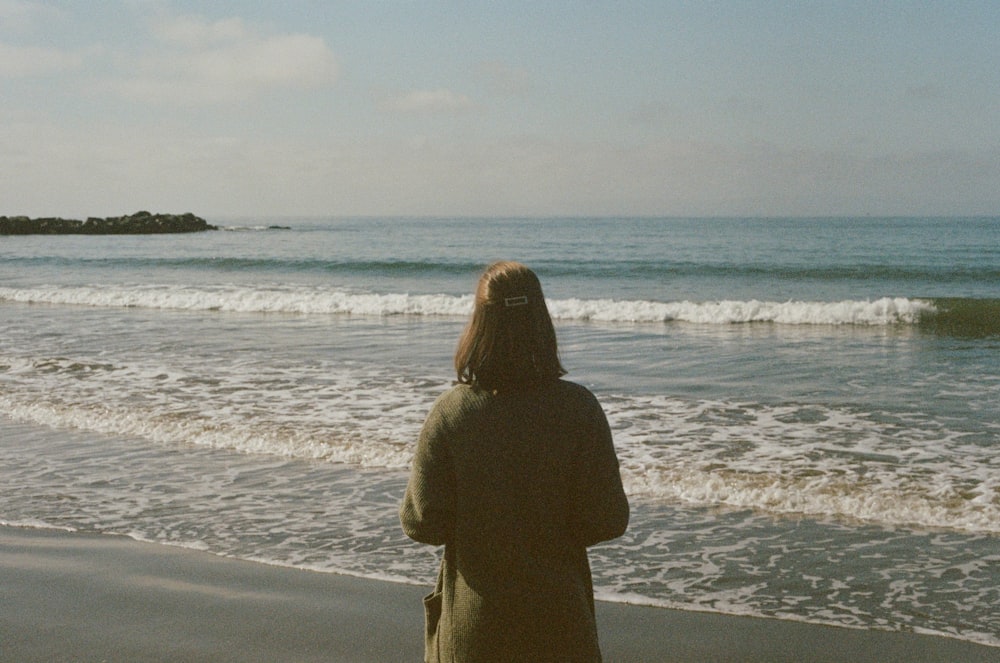 donna in cappotto marrone in piedi sulla spiaggia durante il giorno