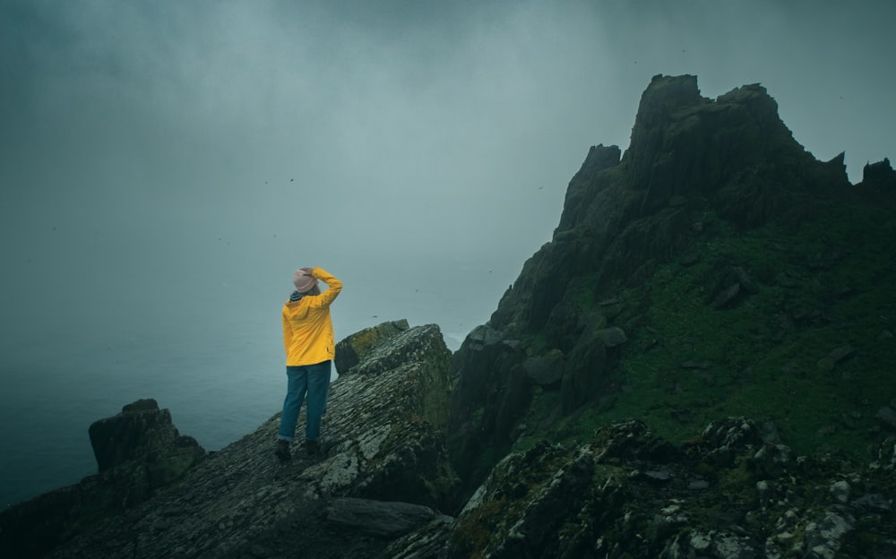 岩の上に立っている黄色いシャツの男