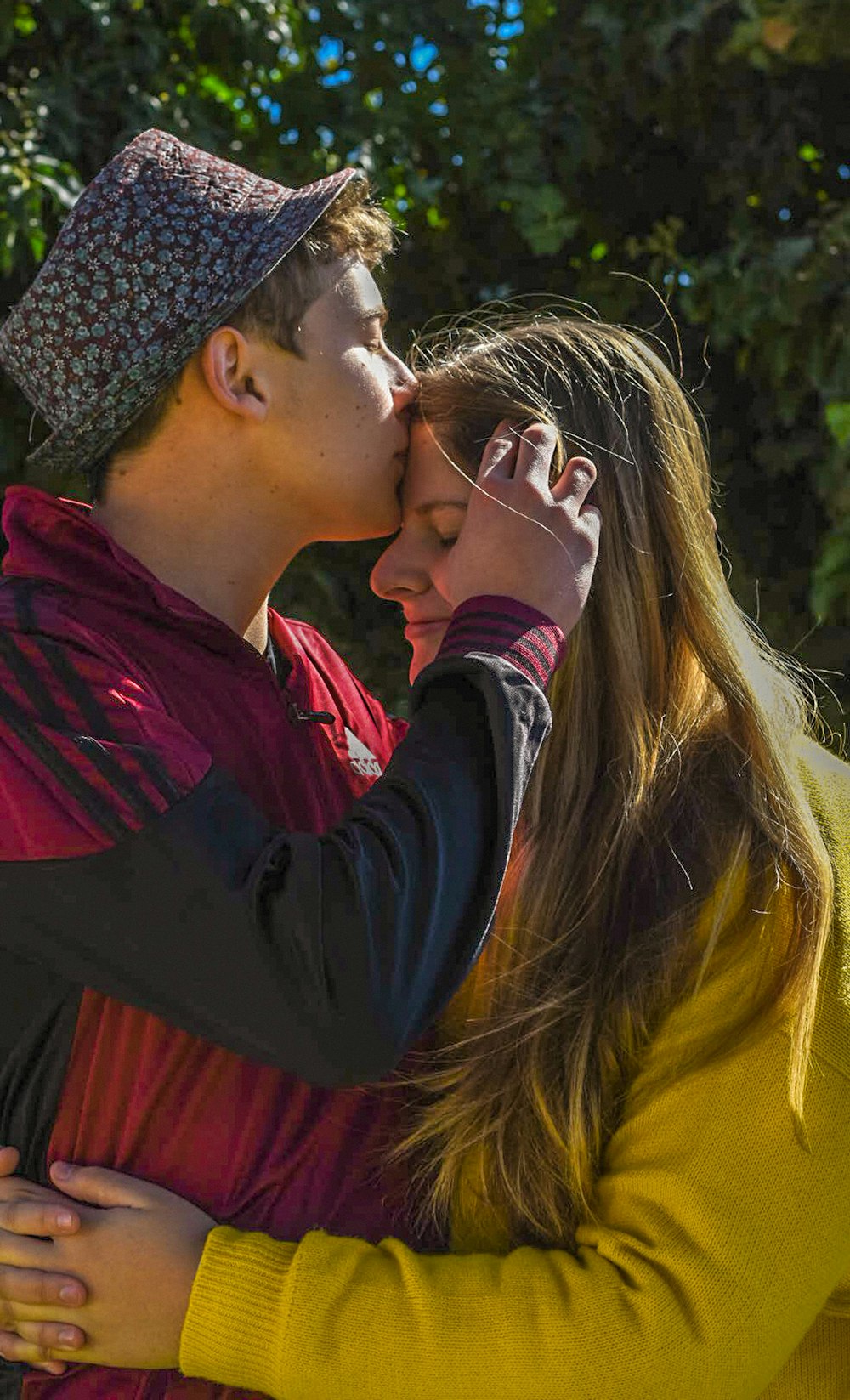 woman in red long sleeve shirt kissing woman in black and white knit cap