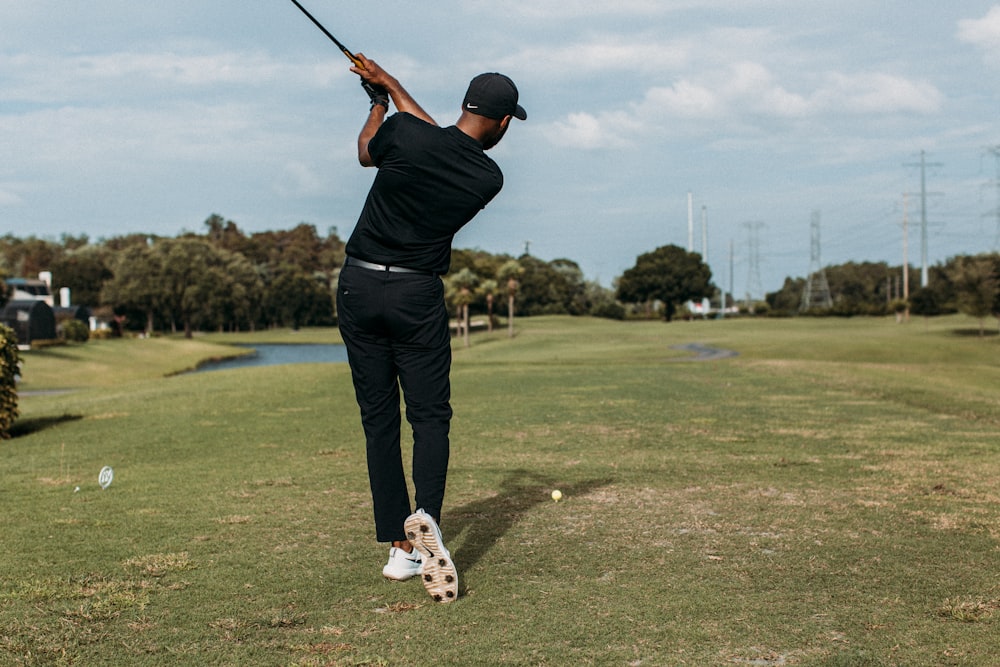 Hombre con camisa negra y pantalones negros jugando al golf durante el día