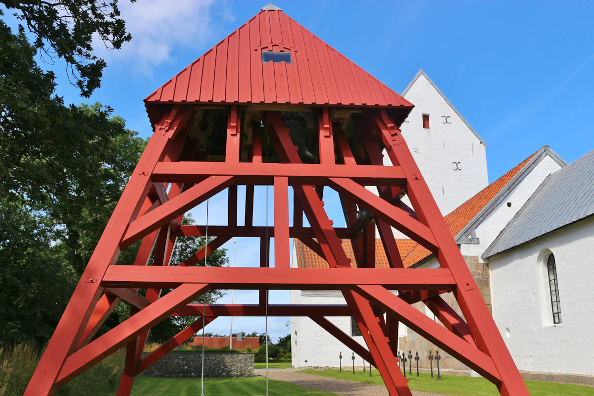 Red timber bell tower standing beside a whitewashed Scandinavian church
