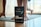 A pouch of Resilience CBD Gummies is prominently displayed on a wooden floor, with a person in the background in a yoga pose or exercise position on a mat. The setting is indoors with natural light coming through a window.