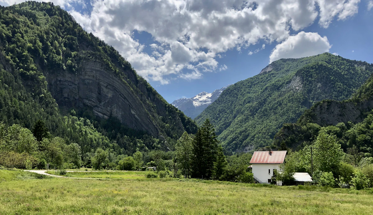 A green meadow and a house below steep wooded mountains at Allemond