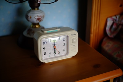 A modern white LED alarm clock displaying time with bright blue digits on a bedside table.