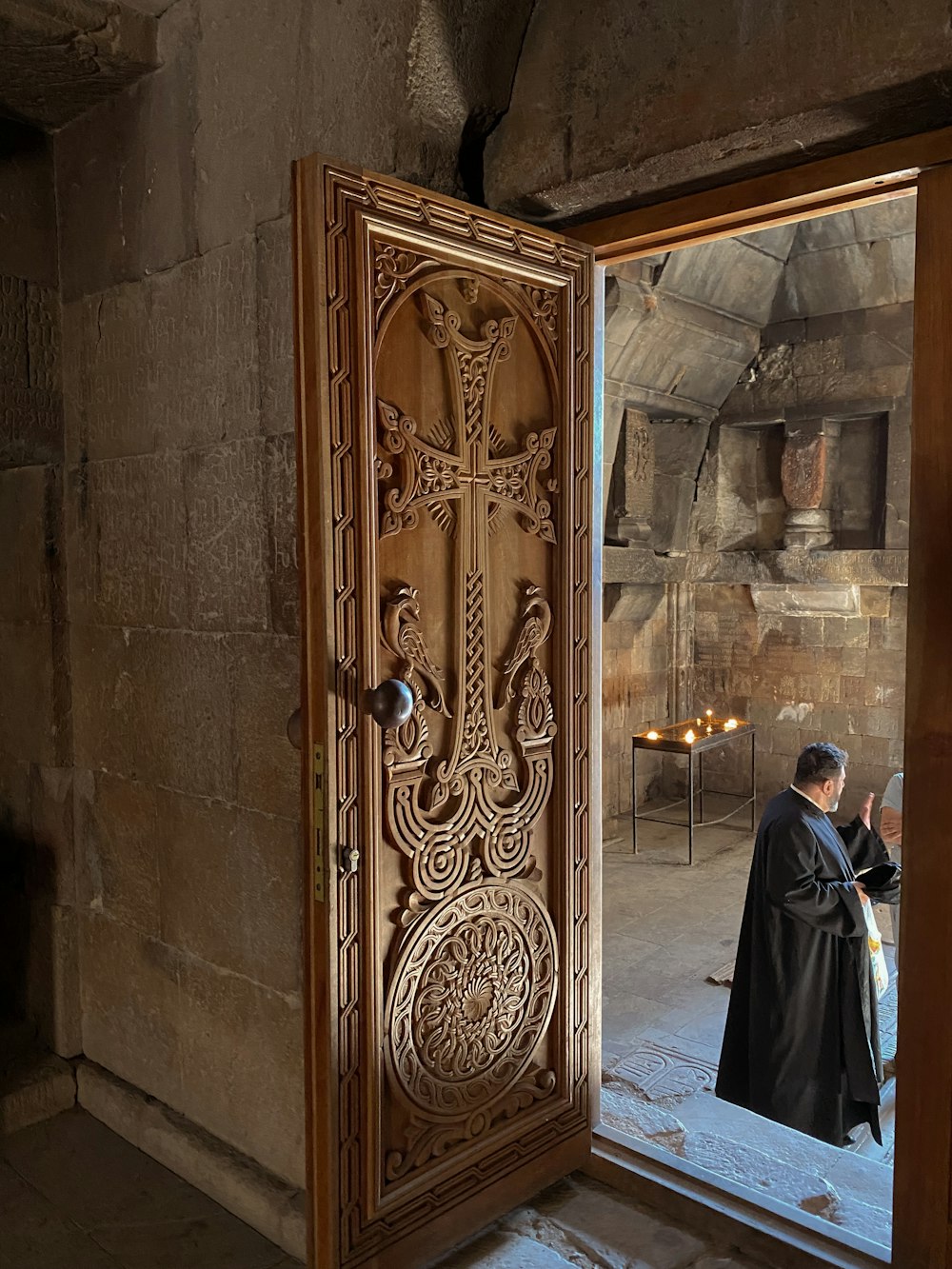 man in black and white robe standing beside brown wooden door