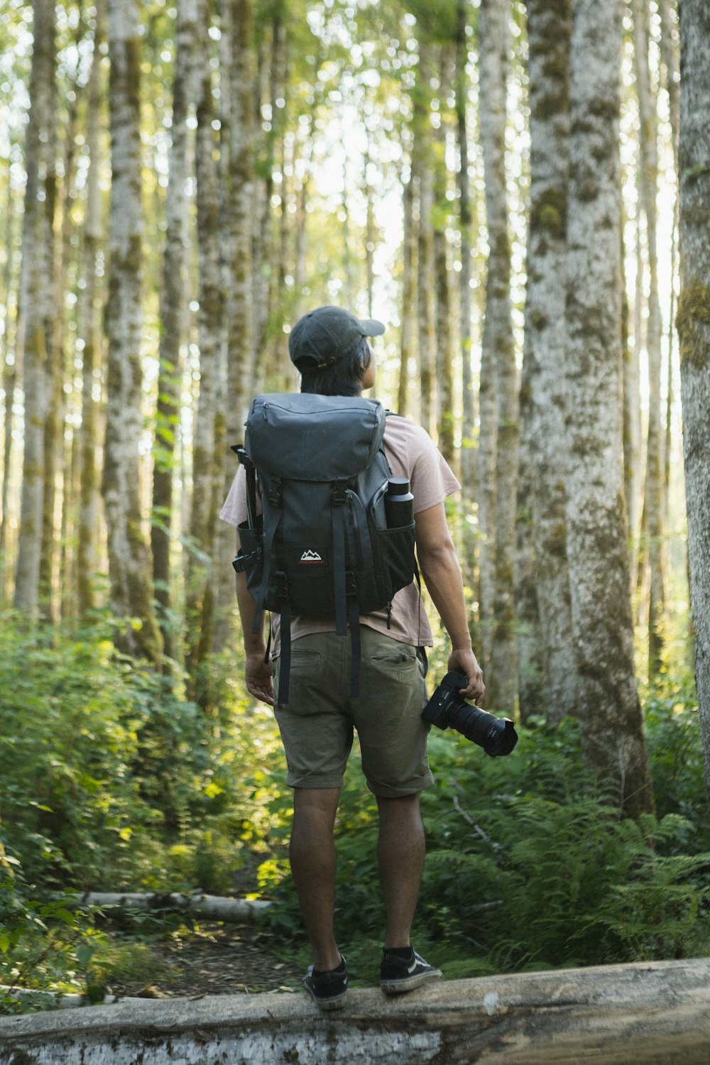 man in black t-shirt and green shorts carrying backpack walking on forest during daytime
