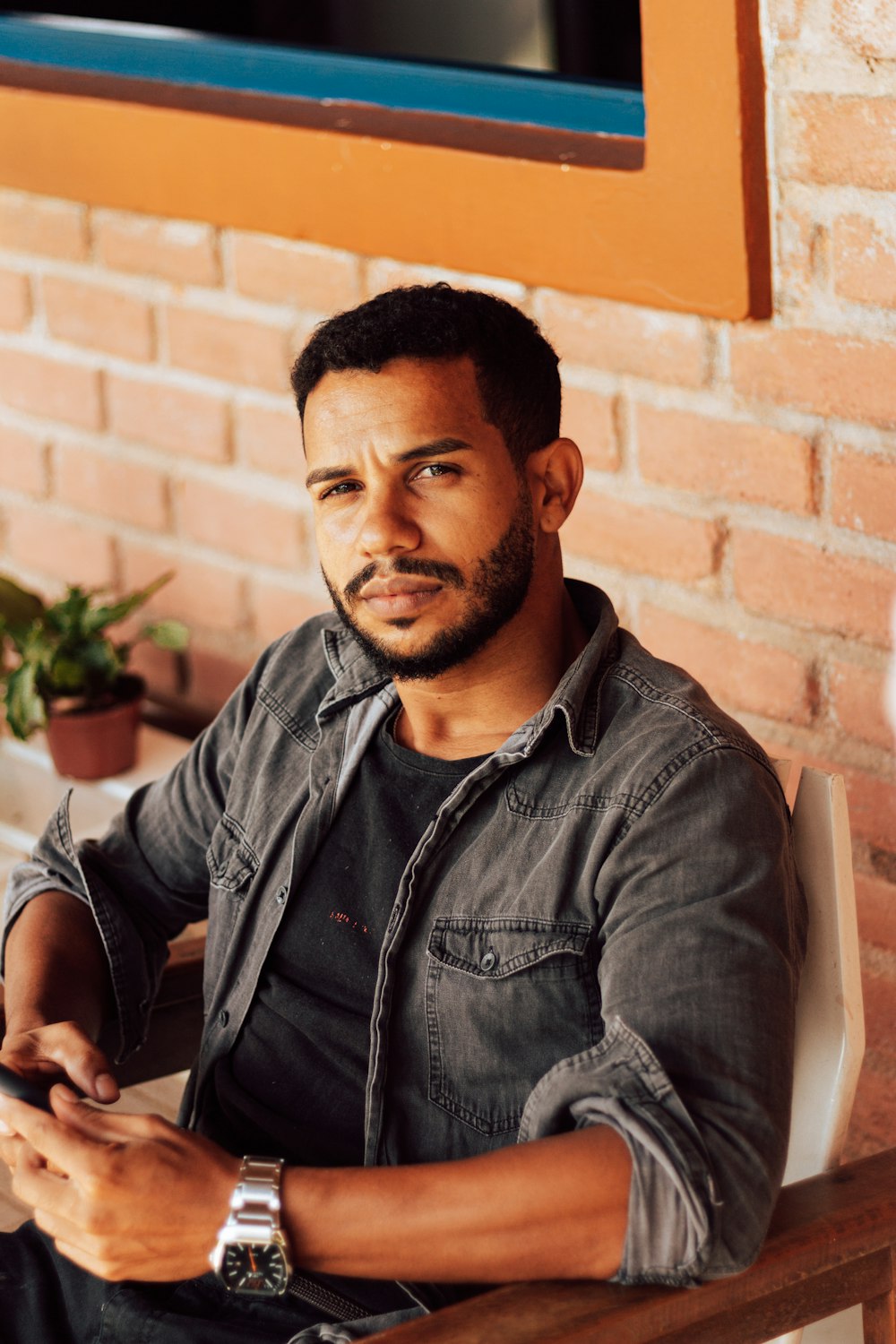 man in black zip up jacket sitting beside brown brick wall