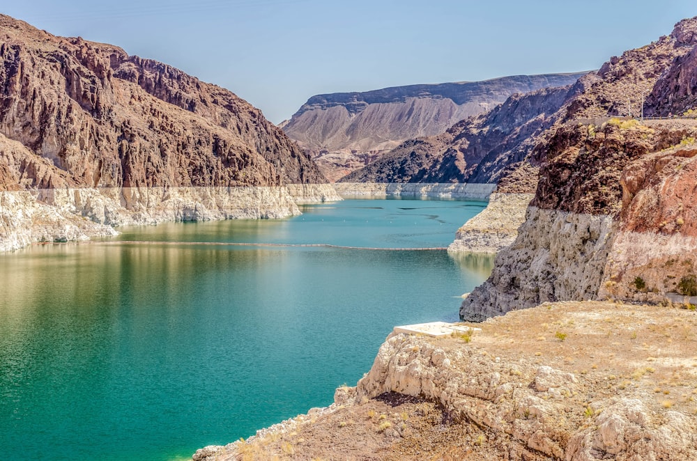 blue lake between brown and gray mountains during daytime